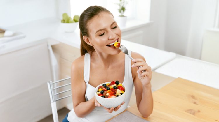 Smiling woman enjoying a fresh fruit salad, highlighting healthy eating tips for maintaining oral health during the holidays in San Francisco, CA.